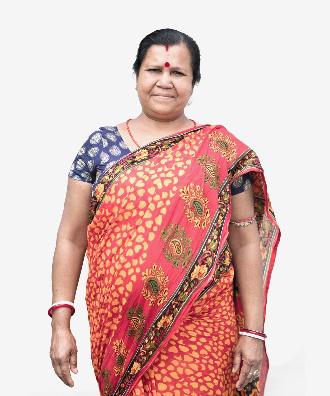 An Indian woman standing and smiling, dressed in brightly coloured traditional clothing of red and blue.