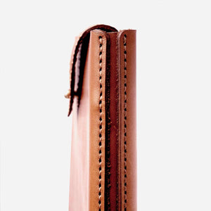 close up image of a camel brown leather laptop sleeve featuring stitching detail and raw leather edges.