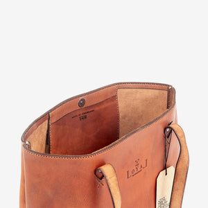 cropped image of a large brown leather tote showing the inside of the bag with a pocket and stainless steel hardware closure.